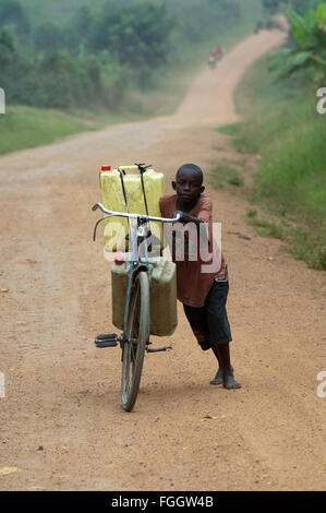 Ragazzo spingendo una bicicletta laden con pieno di acqua contenitori lungo una strada polverosa, Uganda. Foto Stock