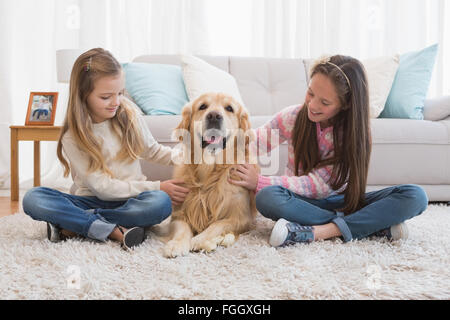 Sorridente sorelle petting loro golden retriever su rug Foto Stock