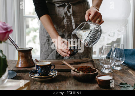 Una donna sta versando il caffè in una tazza per fare il caffè turco. Foto Stock