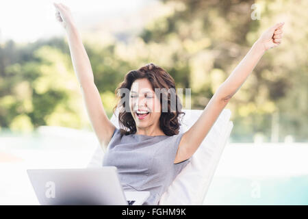 Excited donna giovane utilizzando laptop vicino al bordo della piscina Foto Stock