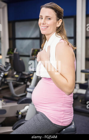 Sorridente donna incinta seduta sulla cyclette Foto Stock