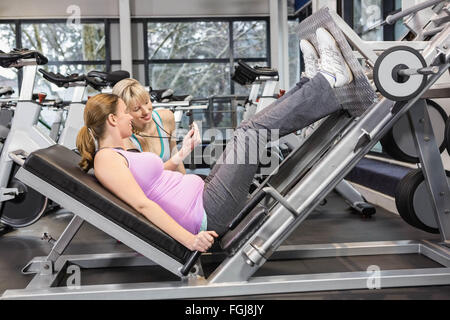 Trainer per motivare la donna incinta mentre utilizzando leg press Foto Stock