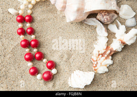 Conchiglie e collana rosso sulla sabbia in spiaggia Foto Stock