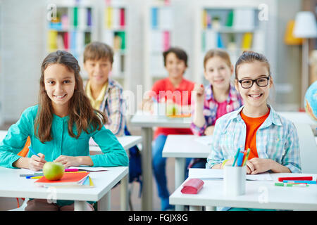 Felice gli alunni seduto da scrivania a lezione Foto Stock