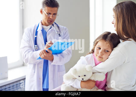 Ragazza carina abbracciando la madre in ospedale durante la visita al medico Foto Stock