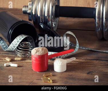 La proteina del siero di latte in polvere in scoop con vitamine e agitatore in plastica su sfondo di legno. Foto Stock