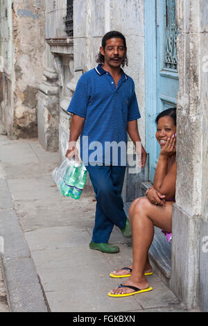 La vita quotidiana a Cuba - sorridenti donna cubana seduto sulla porta di casa a portale con uomo in piedi vicino sulla strada a l'Avana, Cuba West Indies Caraibi Foto Stock