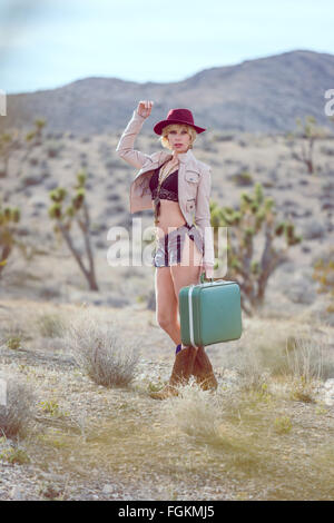 Moda Donna traveler camminando con la valigia e bagagli nel deserto Foto Stock