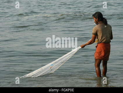 Un giovane pescatore indiano di fumare in un lungi hawling tirando nella sua rete da pesca dalla spiaggia, India Foto Stock