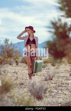 Moda Donna traveler camminando con la valigia e bagagli nel deserto Foto Stock