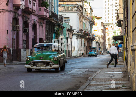 Un verde old timer visto presto una mattina su una strada posteriore a L'Avana, circondato da bellissimi colori pastello edifici robusti. Foto Stock