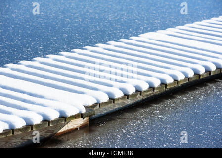 Linee parallele di neve su un molo in legno in acqua congelata in inverno. Foto Stock