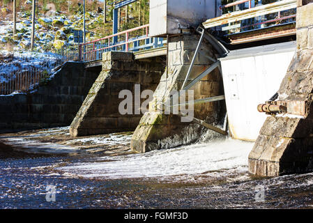 Un trafilamento di acqua fuoriesce sotto una chiusa saracinesca in corrispondenza di una piccola diga idroelettrica. Foto Stock