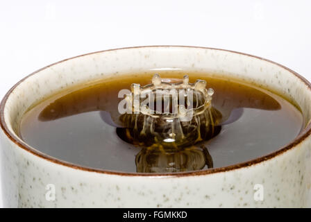 Goccia di latte di cadere nella tazza di caffè nero di miscelazione e di schizzi di goccioline di discesa creazione di motivi forme Increspature nella superficie tazza da tè Foto Stock