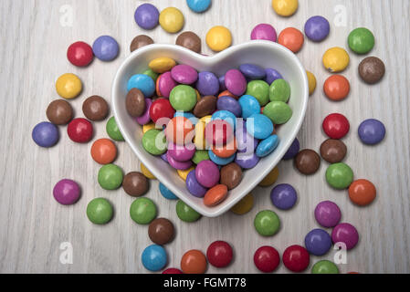 Cioccolato colorato Smarties in un cuore bianco a forma di piatto, vaso Foto Stock