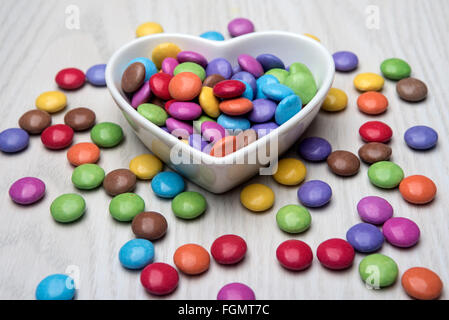 Cioccolato colorato Smarties in un cuore bianco a forma di piatto, ciotola. Foto Stock