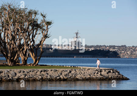 Donna che cammina nel porto di tonno Park con USS Carl Vinson in background, San Diego, California Foto Stock