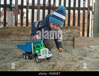 Little Boy giocare nel contenitore di sabbia con colore giocattolo auto Foto Stock