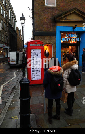 Turisti asiatici guardando un preventivo sul vecchio telefono rosso scatola, Seven Dials, vicino al Covent Garden di Londra, Inghilterra Foto Stock