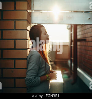 Giovane donna in piedi su una strada con gli occhi chiusi nella luce del tramonto. Il fuoco selettivo Lens Flare. Foto Stock