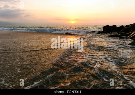 Seascape tramonto è un tramonto sulla spiaggia con rocce di grandi dimensioni in primo piano e un ambiente caldo Cielo di tramonto sull'oceano orizzonte. Foto Stock