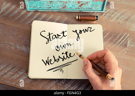 Effetto retrò e tonico immagine di una donna la scrittura a mano una nota con una penna stilografica su un notebook. Concetto motivazionale con il testo scritto a mano INIZIA IL PROPRIO SITO WEB Foto Stock