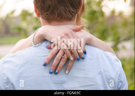 Amare giovane donna sta con le braccia intorno al suo collo, vista sulla sua spalla del suo viso Foto Stock