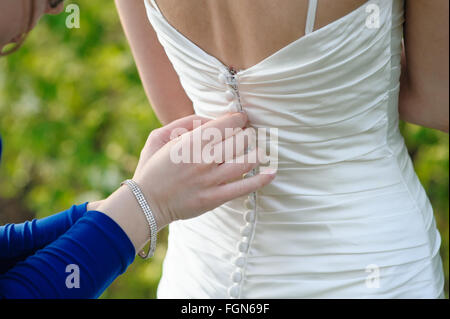 Damigella sta aiutando la sposa di vestire Foto Stock