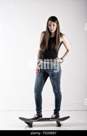 Bella bruna donna in piedi su uno skateboard promuovere uno stile di vita attivo. Foto Stock