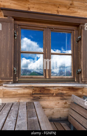 Paesaggio di montagna è riflessa nella finestra di un legno rustico rifugio di montagna. Preso in formato verticale. Foto Stock