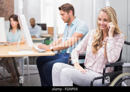 Donna in carrozzella sorride alla telecamera di fronte a persone che lavorano Foto Stock