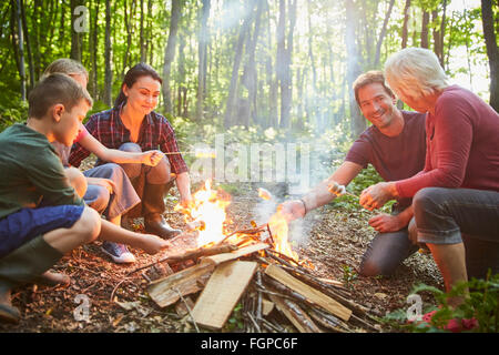Multi-generazione di torrefazione della famiglia marshmallows al falò in foresta Foto Stock