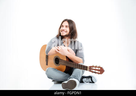 Allegro bel giovane con capelli lunghi sorridente e tenendo la chitarra su sfondo bianco Foto Stock