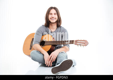 Felice attraente giovane con chitarra seduto e sorridente su sfondo bianco Foto Stock