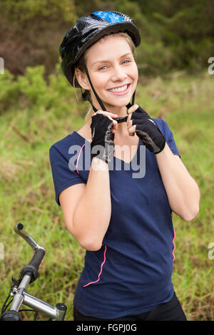 Sorridente bionda atletica mettendo sul casco Foto Stock