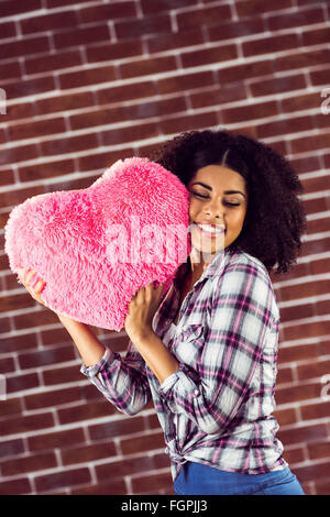 Attraente giovane donna cuddling con cuore-cuscino sagomato Foto Stock