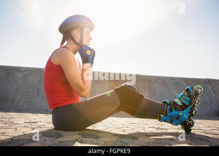 Sportivo skater bionda seduta sul terreno e casco di fissaggio Foto Stock