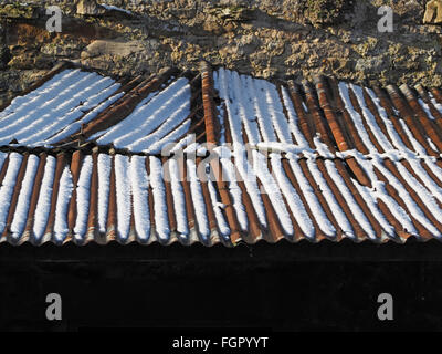 Vecchio corrugarono tin roof sulla fattoria in pietra edificio con neve in incavi arrugginito Foto Stock