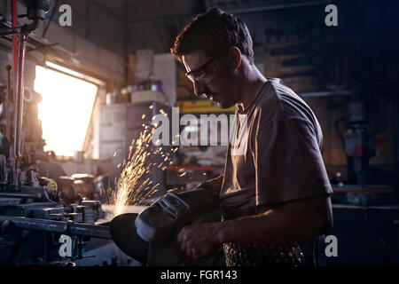 Fabbro utilizzando sander in forge Foto Stock