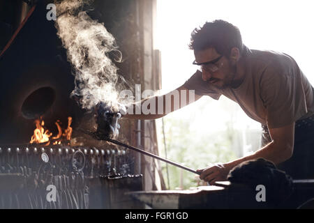 Fabbro per la cottura a vapore di sagomatura del ferro battuto nella fucina Foto Stock