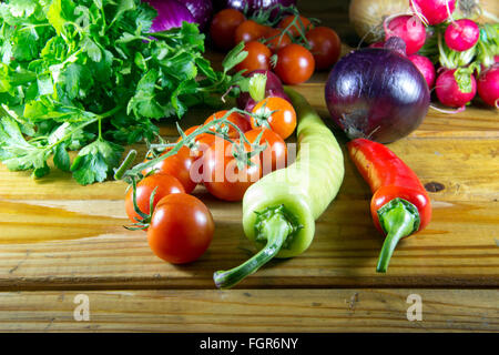 Peperoni, pomodori, Rafano, prezzemolo e cipolla sparsi su un vecchio tavolo in legno Foto Stock