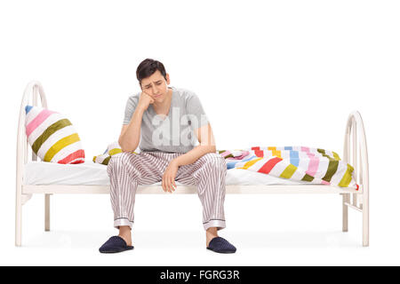 Triste giovane uomo seduto su un letto e contemplando isolati su sfondo bianco Foto Stock