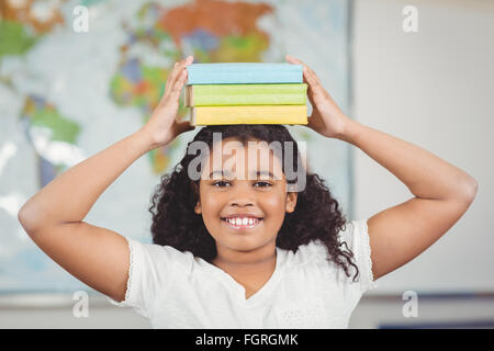 Pupilla sorridente libri di bilanciamento sulla testa in una classe Foto Stock