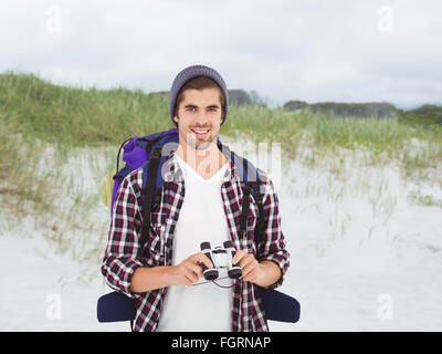 Immagine composita di felice hipster indossando uno zaino tenendo il binocolo Foto Stock