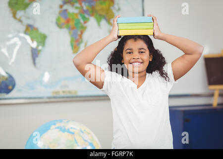 Pupilla sorridente libri di bilanciamento sulla testa in una classe Foto Stock