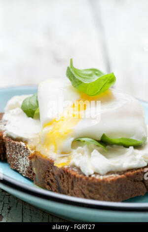 Toast con uovo in camicia, il formaggio e le foglie di basilico su uno sfondo di legno Foto Stock
