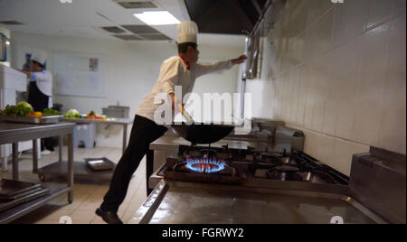 Chef nella cucina dell'hotel di preparare il cibo con il fuoco Foto Stock