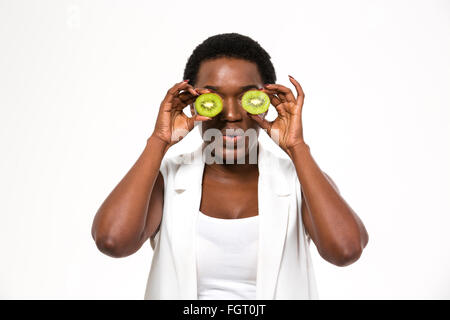 Funny divertente americano africano giovane donna holding kiwi metà davanti agli occhi su sfondo bianco Foto Stock