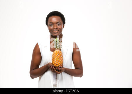 Sorridente piuttosto americano africano giovane donna in piedi e tenendo ananas su sfondo bianco Foto Stock