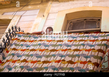 La vita quotidiana a Cuba - donna cubana guardando in giù sul foglio appeso fuori ad asciugare sul balcone a L'Avana, Cuba, West Indies, dei Caraibi e America centrale Foto Stock